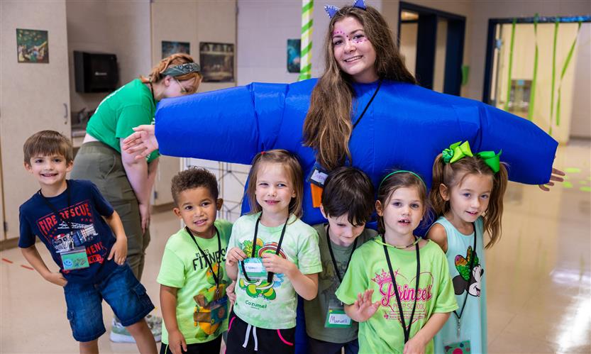 A girl in an inflatable suit takes a picture with young students